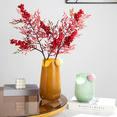Amber glass vase with accent bubble, holding bright red berry branches, infusing home with vibrant and healing atmosphere.