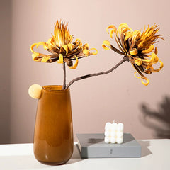 Amber handmade glass vase filled with decorative yellow chrysanthemums, illuminating space with an emotional and cozy ambiance.