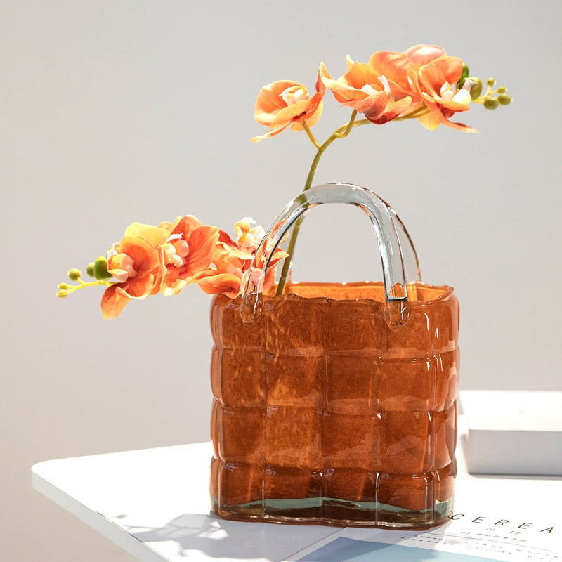 Amber-colored handbag glass vase with vibrant flowers on white table