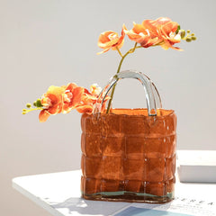 Amber-colored handbag glass vase with vibrant flowers on white table