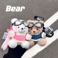 Pink and blue dressed aviator bear plush keychains, side by side, held outdoors with street background