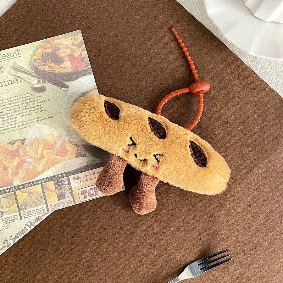 Baguette plush keychain lying near a magazine and a fork, with a cute face