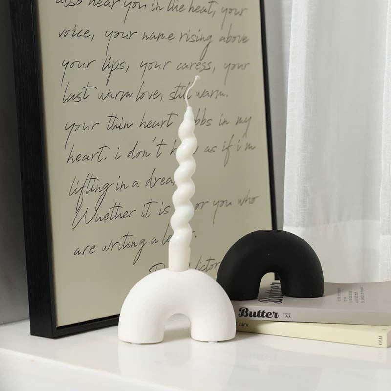 Black and white half arch ceramic candle holders arranged by a window with artistic text background