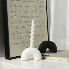 Black and white half arch ceramic candle holders arranged by a window with artistic text background