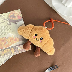 Blushing croissant plush keychain placed on a brown tabletop next to a magazine