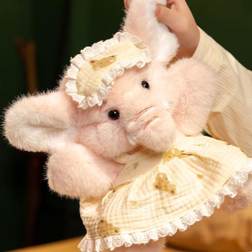 A hand gently lifts the pink Bruce Comfort Sitting Elephant Plush to reveal its plush softness and huggability.