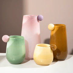 Set of four candy color glass vases in pink, green, yellow, and amber, each adorned with a matching accent bubble, displaying modern and artistic decor.