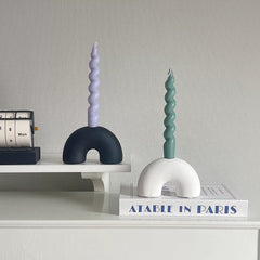 Unique ceramic candle holders in black and white holding colorful spiral candles, placed stylishly on a bookshelf