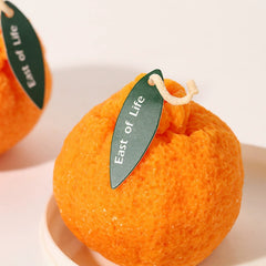 Close-up of ugly tangerine candle featuring "East of Life" green leaf tag
