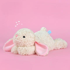 Creamy white bunny plush toy with soft pink ears, lying on pink background