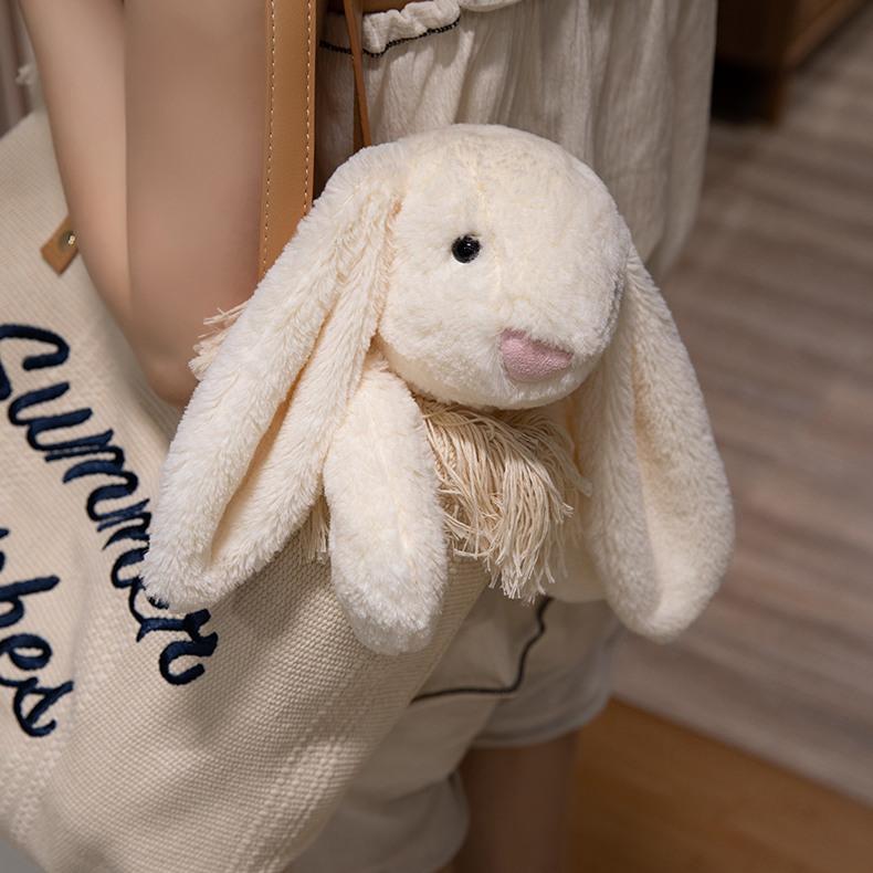 Cream-colored lop-eared bunny plush hanging adorably from a summer-themed bag, radiating soft companionship.