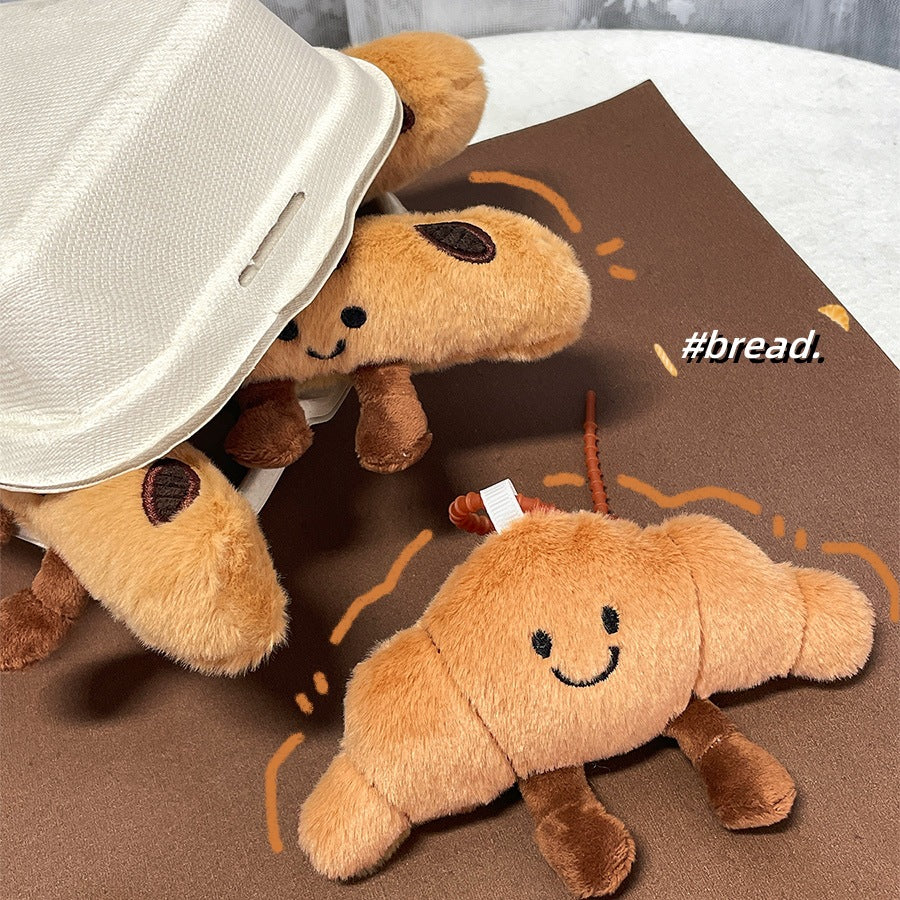 Croissant-shaped plush keychain emerging from a box with illustrated accents