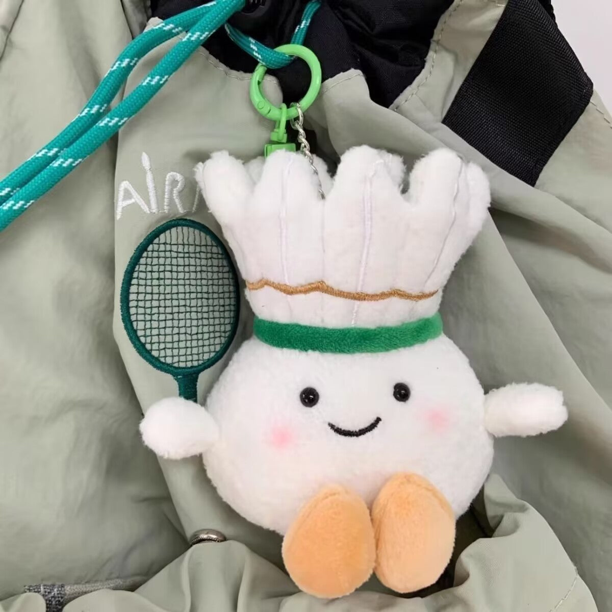 Cute shuttlecock plush keychain clipped to a green sports bag, displaying a charming smile and soft details.