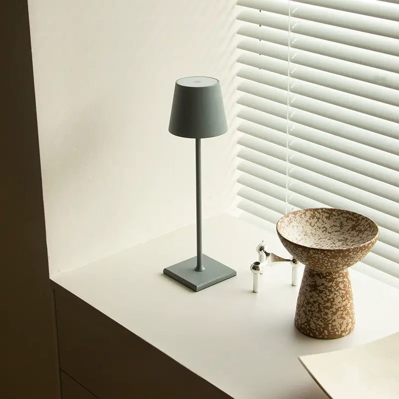 Gray minimalist desk lamp placed on a windowsill beside artistic decor in a bright room