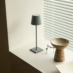Gray minimalist desk lamp placed on a windowsill beside artistic decor in a bright room