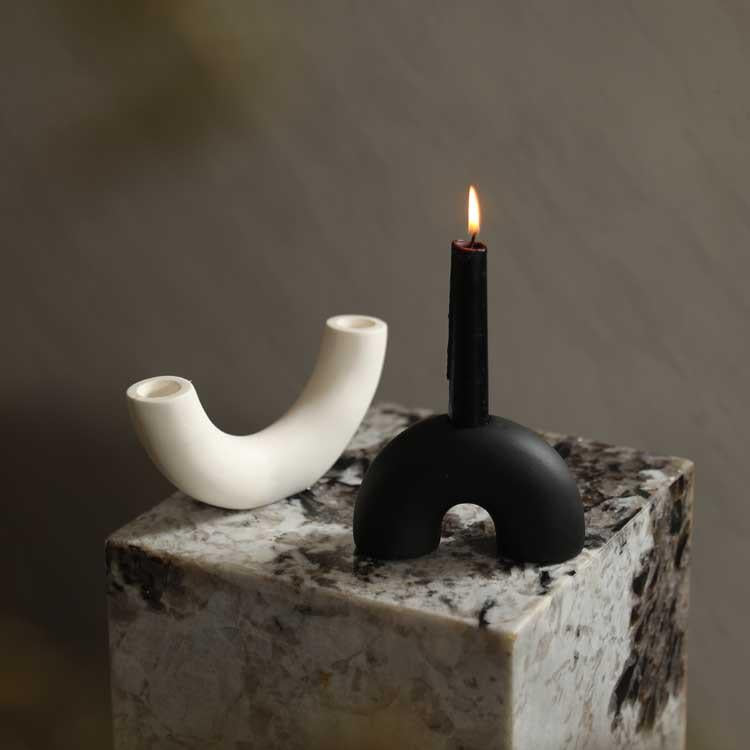 Black and white ceramic candle holders, one with a lit candle, displayed on a marble surface