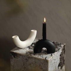 Black and white ceramic candle holders, one with a lit candle, displayed on a marble surface