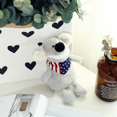 Grey plush toy with a big toothy grin and patriotic scarf, positioned by a vase and leafy plant