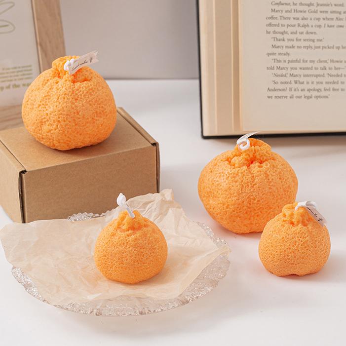 Multiple ugly tangerine shaped candles next to a kraft box and open book