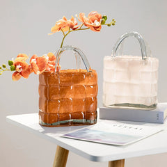 Elegant handbag glass vases in white and amber displayed together with fresh orange orchids