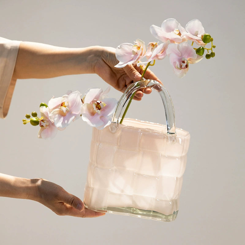 Person holding handbag-shaped glass vase with blooming pink flowers