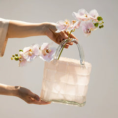 Person holding handbag-shaped glass vase with blooming pink flowers