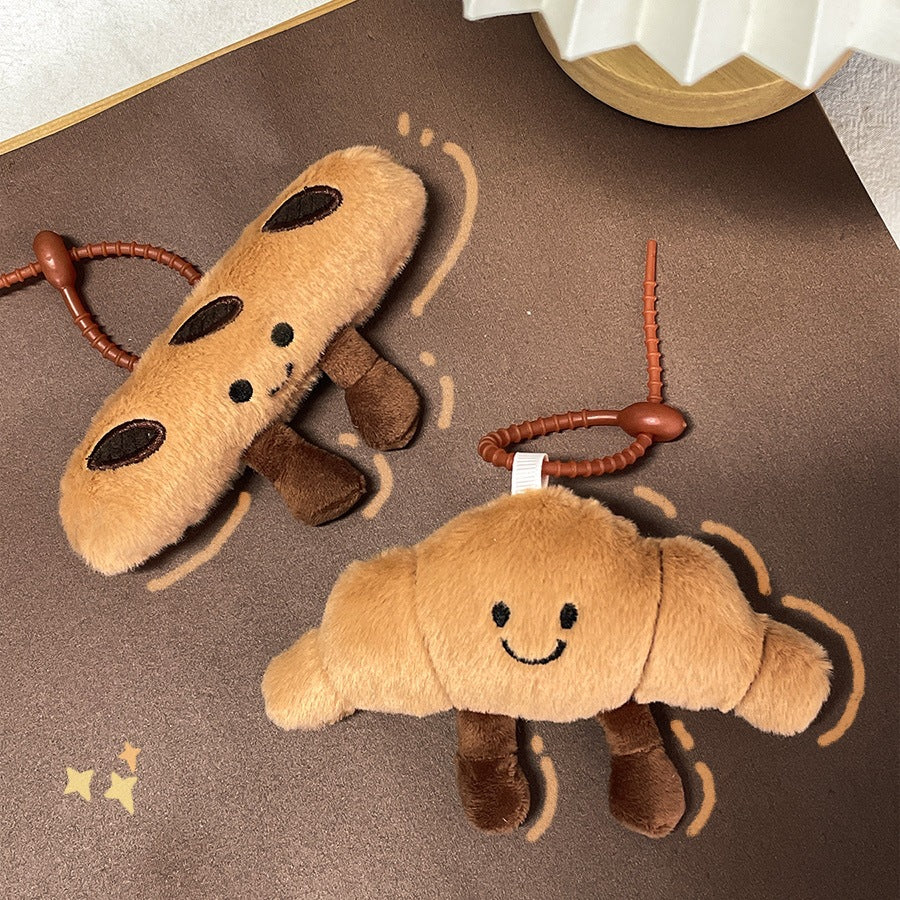 Croissant and baguette plush keychains with playful designs on a starry brown background
