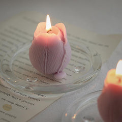Lit lilac tulip candle resting on a clear glass tray beside a letter.