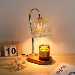 Candle warmer lamp with floral glass shade, golden stem, and wooden base warming an amber scented candle
