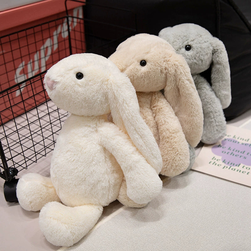 Three lop-eared bunny plush toys lined up next to a wire basket, ready to be chosen for supportive companionship.
