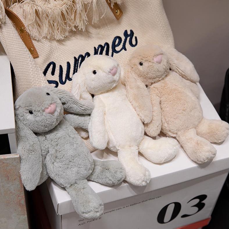 Three plush lop-eared bunny toys in gentle gray, cream, and beige colors displayed together for comfort seekers.
