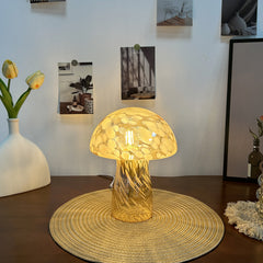 Retro mushroom glass desk lamp emits warm light on a wooden table, surrounded by minimalist decor.