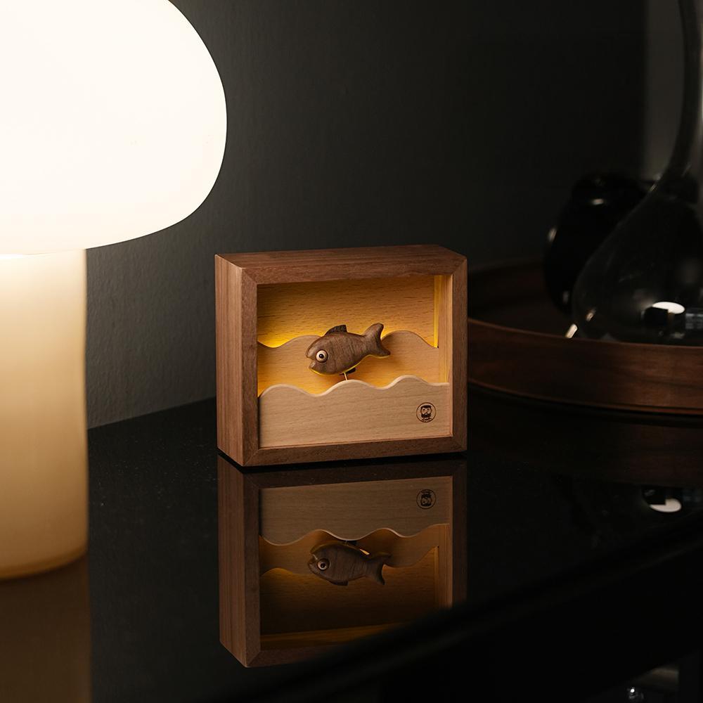 The wooden fish night light illuminated beside a modern lamp, creating a sophisticated ambiance for the home.