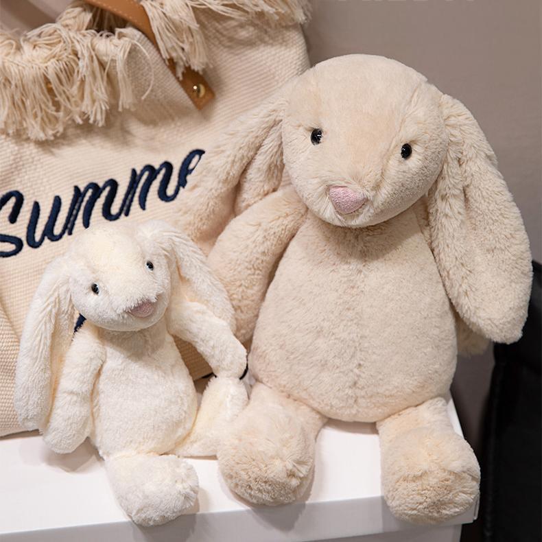 Two lop-eared bunny plush toys of different sizes next to a chic bag, highlighting playful companionship.