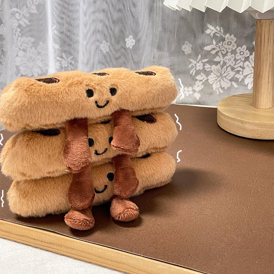 Stacked baguette plush keychains with smiling faces on a wooden tray
