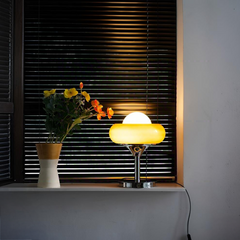 Yellow retro desk lamp glowing warmly on windowsill, alongside floral decoration