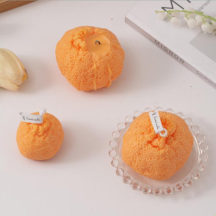 Three ugly tangerine candles in different sizes arranged on a white table