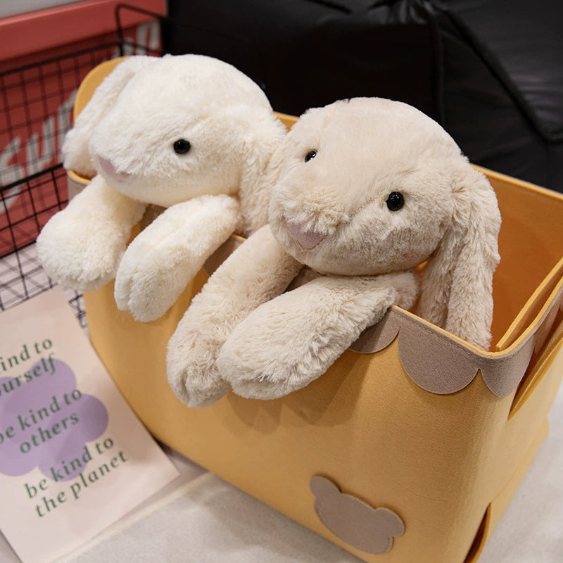 Pair of lop-eared bunny plush toys nestled together in a yellow bin, evoking homey warmth.