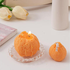 Two ugly tangerine shaped candles, one burning and one unlit, placed on a table