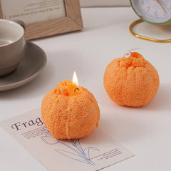 One burning and one unlit ugly tangerine candle near a cup and clock