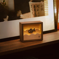 Handcrafted wooden fish night light glowing by an artistic calligraphy backdrop, blending visual inspiration with gentle lighting.
