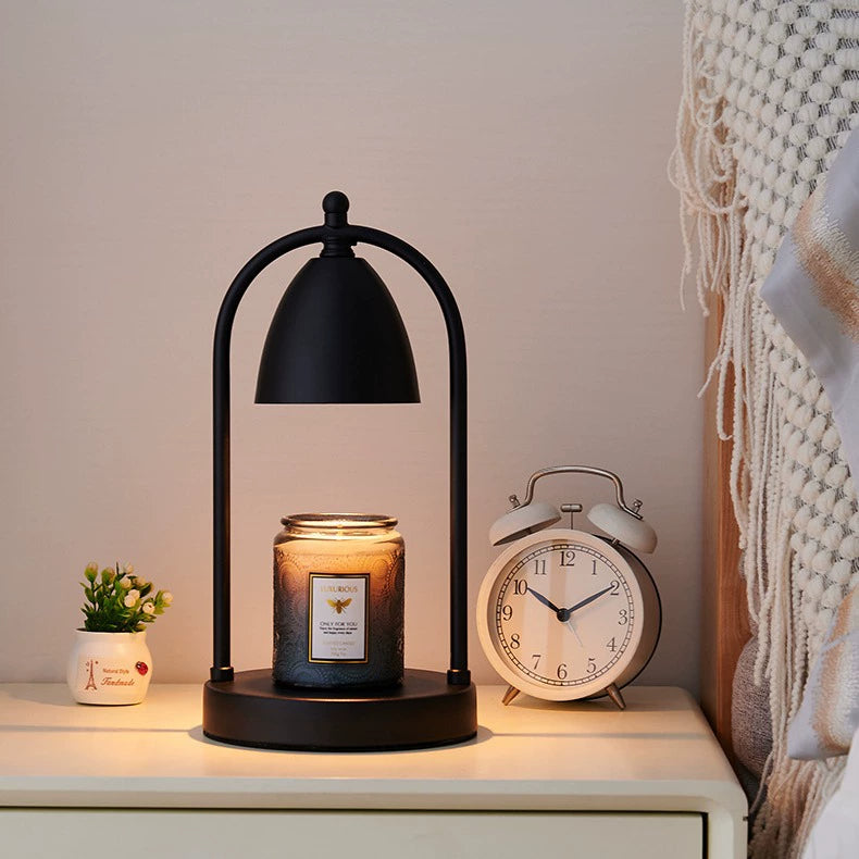 Black vintage candle warmer lamp illuminating a scented candle on a nightstand beside an alarm clock in a calming bedroom setting.
