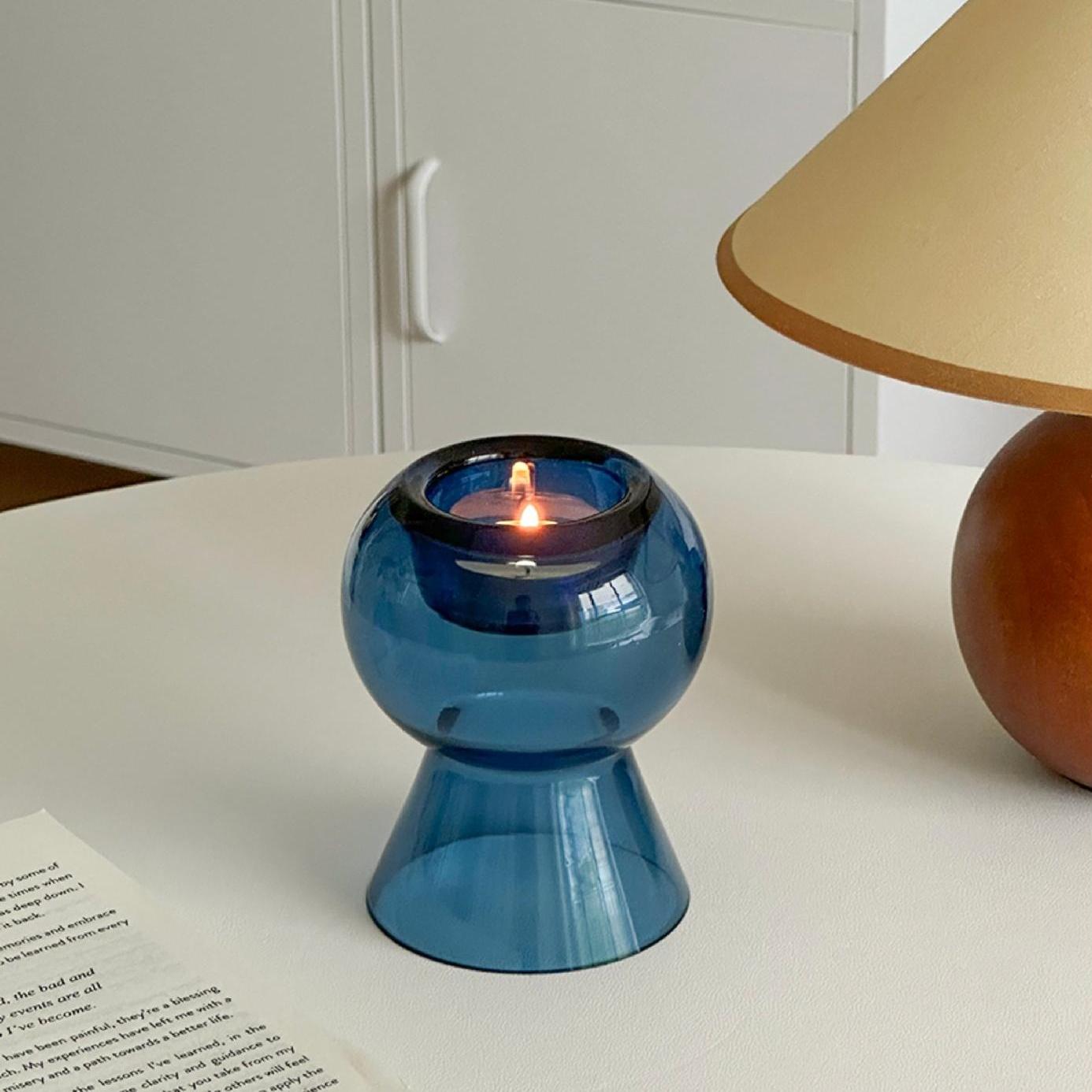 Blue glass candle holder softly glowing next to a classic table lamp.