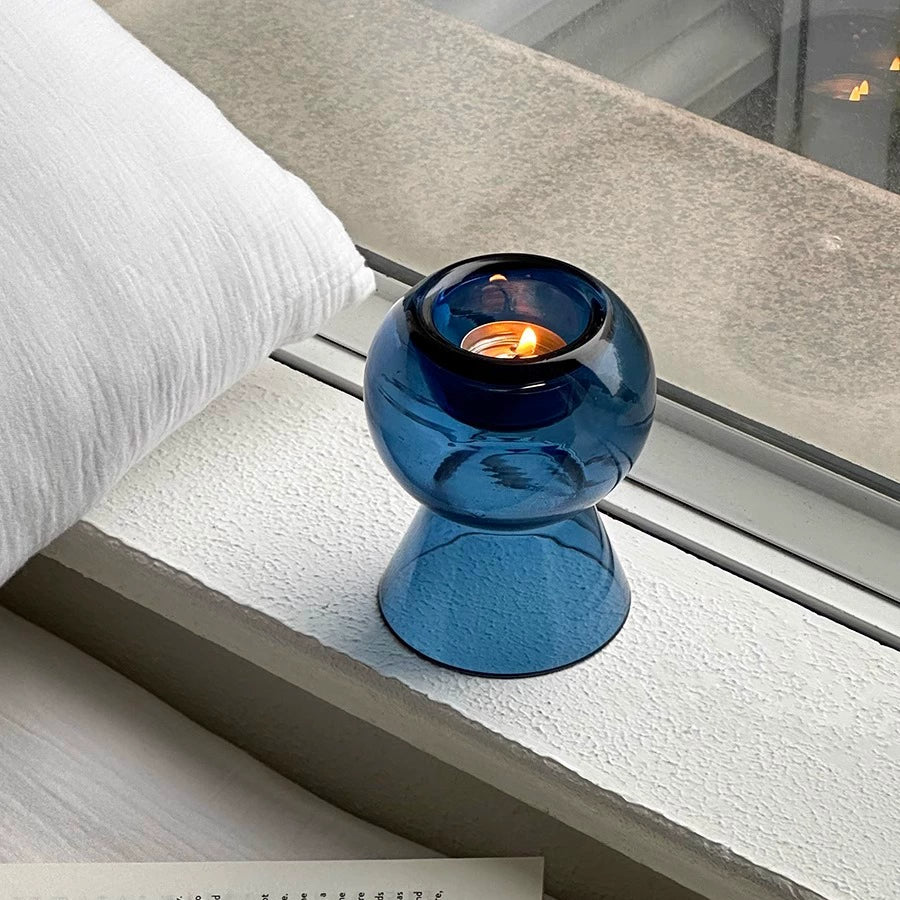 Creative minimalist glass candle holder illuminated by candlelight on a room window sill.