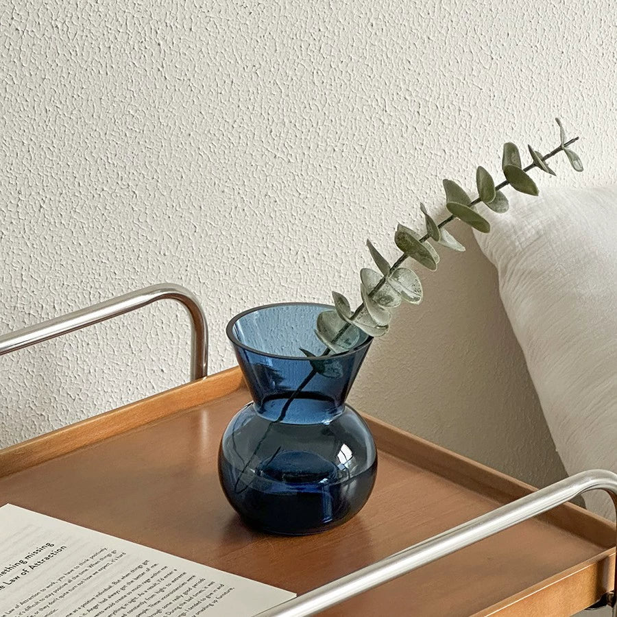 Minimalist blue glass vase holding eucalyptus, complementing the glass candle holder nearby.