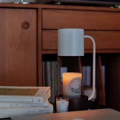 Candle warmer lamp illuminating a scented candle in a cozy study setting surrounded by books