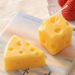 Wedge and cube cheese candles displayed on a book, accented by fruits, perfect as whimsical decor.