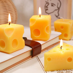 Several cube and wedge cheese candles displayed and burning atop books, creating a warm, cozy ambiance.