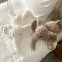 Top view of white and brown elephant plush toys displaying their plush texture and gentle curves on a soft bed.