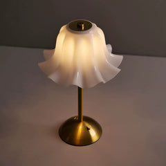 The Floral Grace Minimalist Desk Lamp illuminated with a warm, comforting light, showcasing its gentle flower-shaped shade and elegant brass-colored base on a desk.